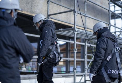 足場で安全帯とヘルメットを着用し作業する3人の作業員。