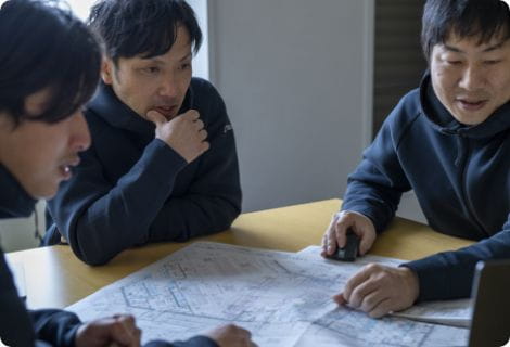 図面とPCを囲み検討する3人の男性